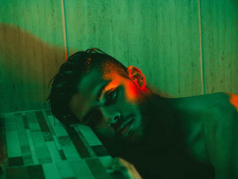 man contemplatively laying side of head on table while staring at camera in a green room