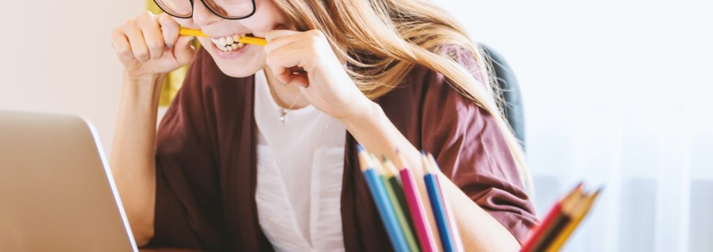 woman biting pencil in front of a laptop