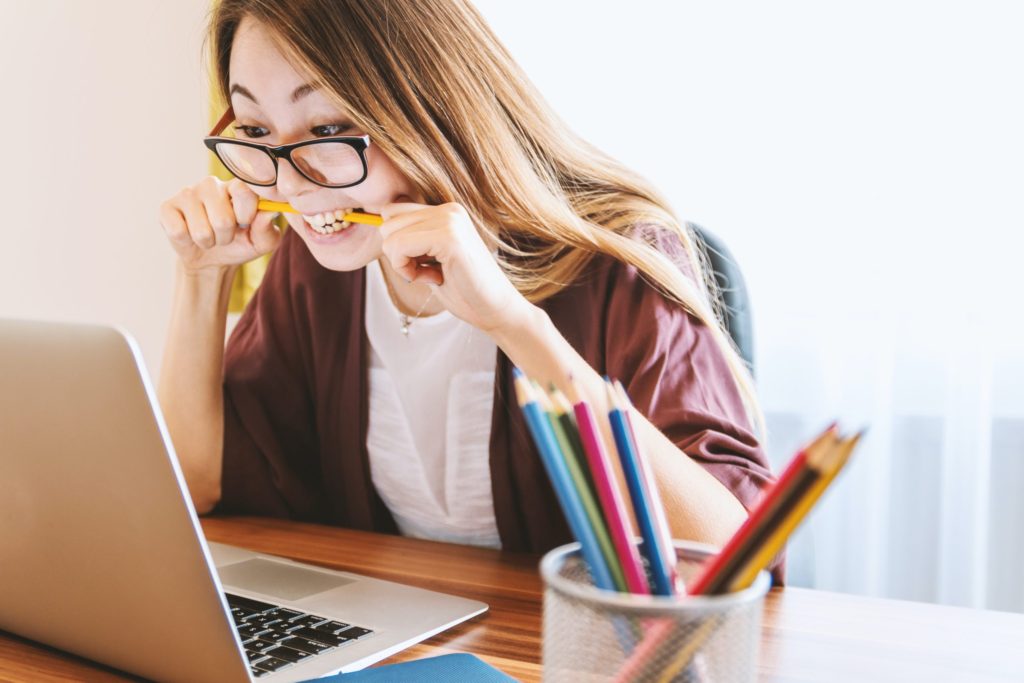 WOMAN BITING HER PENCIL WHILE LOOKING AT LAPTOP